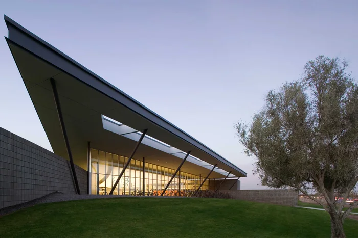 Cesar Chavez Regional Library: a broad sweeping roof plane lifting over a glazed reading room, seen across a lawn.