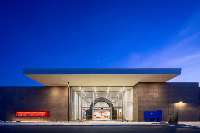 Richard Elías-Mission Library Expansion at night: a dark masonry frontage with a tall lit entrance recess.