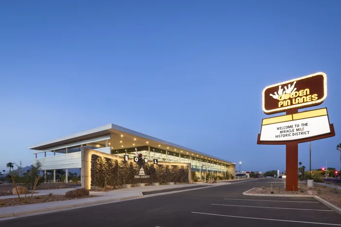 Pima County Northwest Service Center at dusk, its glazed frontage beside a retained mid-century bowling alley sign.
